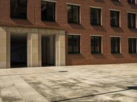 an empty courtyard that is near a brick building and several windows has a street sign on the sidewalk