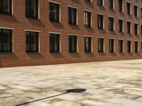 an empty courtyard that is near a brick building and several windows has a street sign on the sidewalk