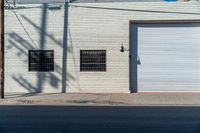 a empty side walk with closed garage doors and one fire hydrant in front of an urban brick wall