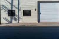 a empty side walk with closed garage doors and one fire hydrant in front of an urban brick wall