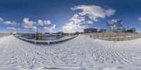 a fisheye view of an empty beach with white snow around it and buildings in the background