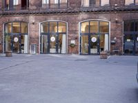 a building with many windows and doors on the sidewalk as a man stands outside near the door