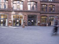 a building with many windows and doors on the sidewalk as a man stands outside near the door