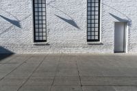 an empty street with two open windows next to a white brick building with black trim