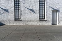 an empty street with two open windows next to a white brick building with black trim