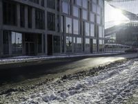 the sun shines brightly in the windows and snow covering street in front of the large building