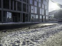 the sun shines brightly in the windows and snow covering street in front of the large building