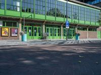 an empty green brick parking lot with people walking near it in front of a green building