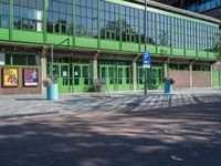 an empty green brick parking lot with people walking near it in front of a green building