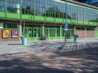 an empty green brick parking lot with people walking near it in front of a green building