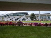 grass and flowers are growing below the sidewalk by an urban building and steps on the right
