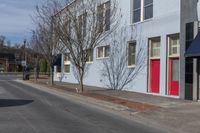 there are a lot of trees in the front of the building, with a blue awning on one side and red door on the other side