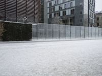 there are a lot of snow on the ground near the fence and some buildings in the background