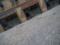 the sidewalk is paved with stones and has a bench in front of it, with no people inside