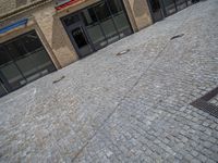 the sidewalk is paved with stones and has a bench in front of it, with no people inside