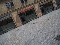 the sidewalk is paved with stones and has a bench in front of it, with no people inside