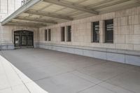 there are two empty windows in this building and the sidewalk has a cement floor with an empty area of cement