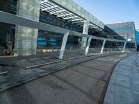 a man walking across a road past a large glass building under a blue sky above him