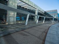 a man walking across a road past a large glass building under a blue sky above him