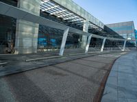 a man walking across a road past a large glass building under a blue sky above him