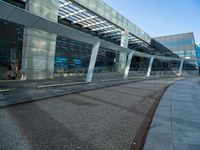 a man walking across a road past a large glass building under a blue sky above him