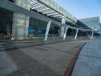 a man walking across a road past a large glass building under a blue sky above him