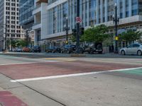 the green paint is painted on a bike path in front of an office building and large, trees