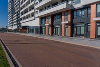 the empty red road is next to tall buildings on the side of the street and people walking outside