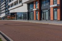 the empty red road is next to tall buildings on the side of the street and people walking outside