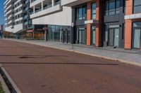 the empty red road is next to tall buildings on the side of the street and people walking outside