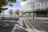 a large glass building next to a brick road with benches, fire hydrants and cars