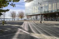 a large glass building next to a brick road with benches, fire hydrants and cars