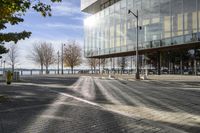 a large glass building next to a brick road with benches, fire hydrants and cars