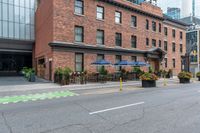 an empty city street with a bunch of plants on the curb and umbrellas on some buildings