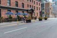 an empty city street with a bunch of plants on the curb and umbrellas on some buildings