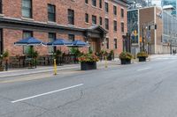 an empty city street with a bunch of plants on the curb and umbrellas on some buildings