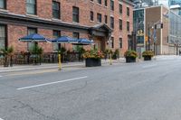 an empty city street with a bunch of plants on the curb and umbrellas on some buildings