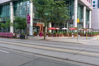 a tall glass building with some people in front and an umbrella covered table next to it