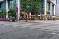 a tall glass building with some people in front and an umbrella covered table next to it