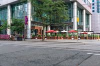 a tall glass building with some people in front and an umbrella covered table next to it