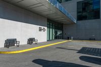 two benches near a large building with a shadow on the sidewalk outside it's entrance