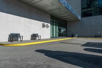 two benches near a large building with a shadow on the sidewalk outside it's entrance