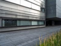 a person on a bench near a building with grass growing inside it and a sidewalk next to it