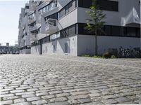 the bricked sidewalk in front of an apartment block in an urban area that contains an old white building with black windows and a white balcony