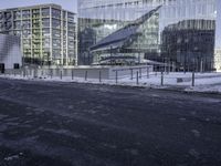 a group of glass office buildings on top of snow covered ground near street with paved road