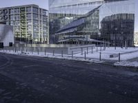 a group of glass office buildings on top of snow covered ground near street with paved road