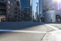 a person is walking across an empty city street in the late afternoon sun and tall buildings