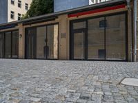 the sidewalk is paved with stones and has a bench in front of it, with no people inside