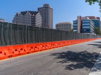 a fence surrounds an empty street with several buildings in the background and a blue sky