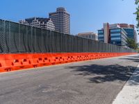 a fence surrounds an empty street with several buildings in the background and a blue sky